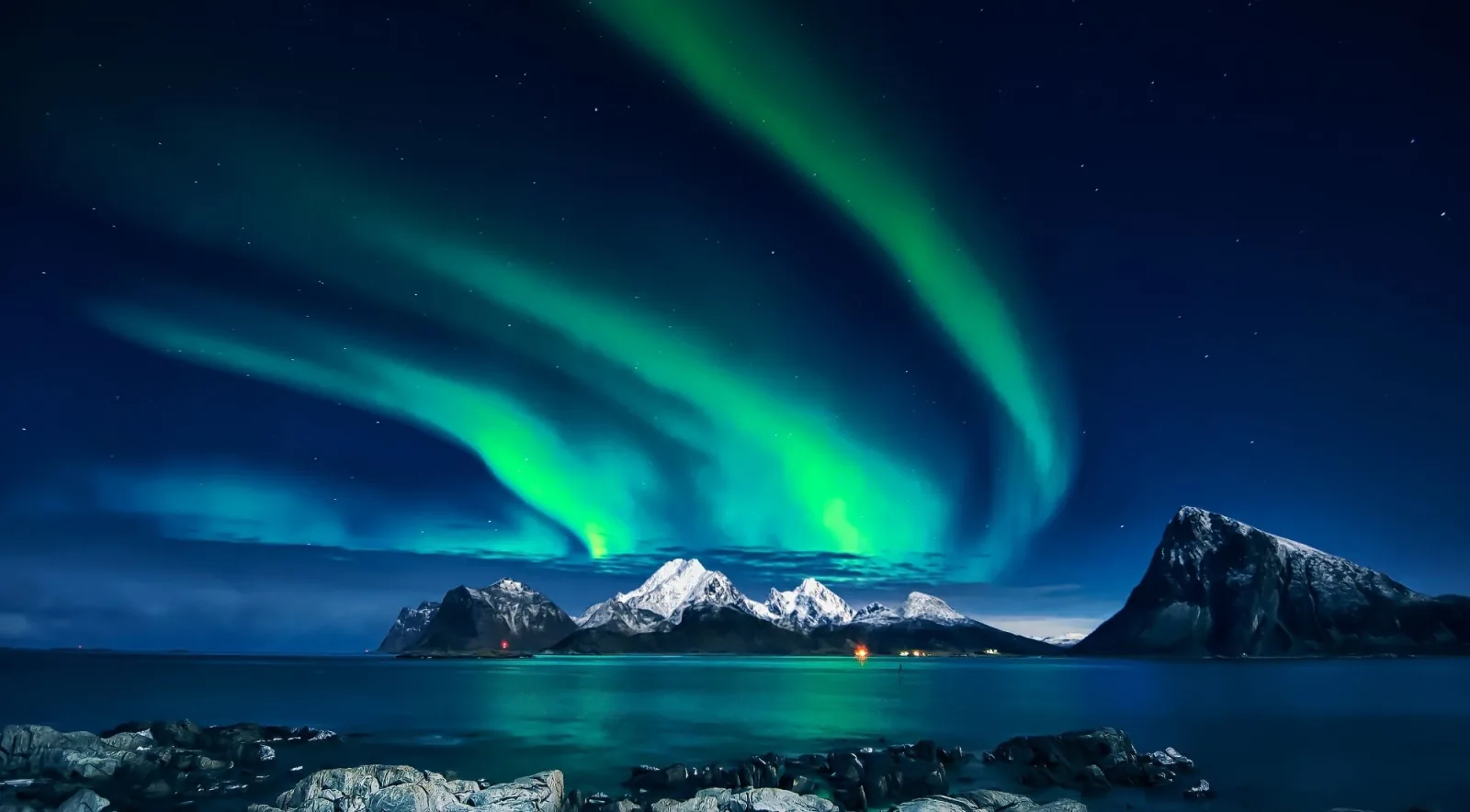Green aurora borealis arcing over snow-capped peaks at night