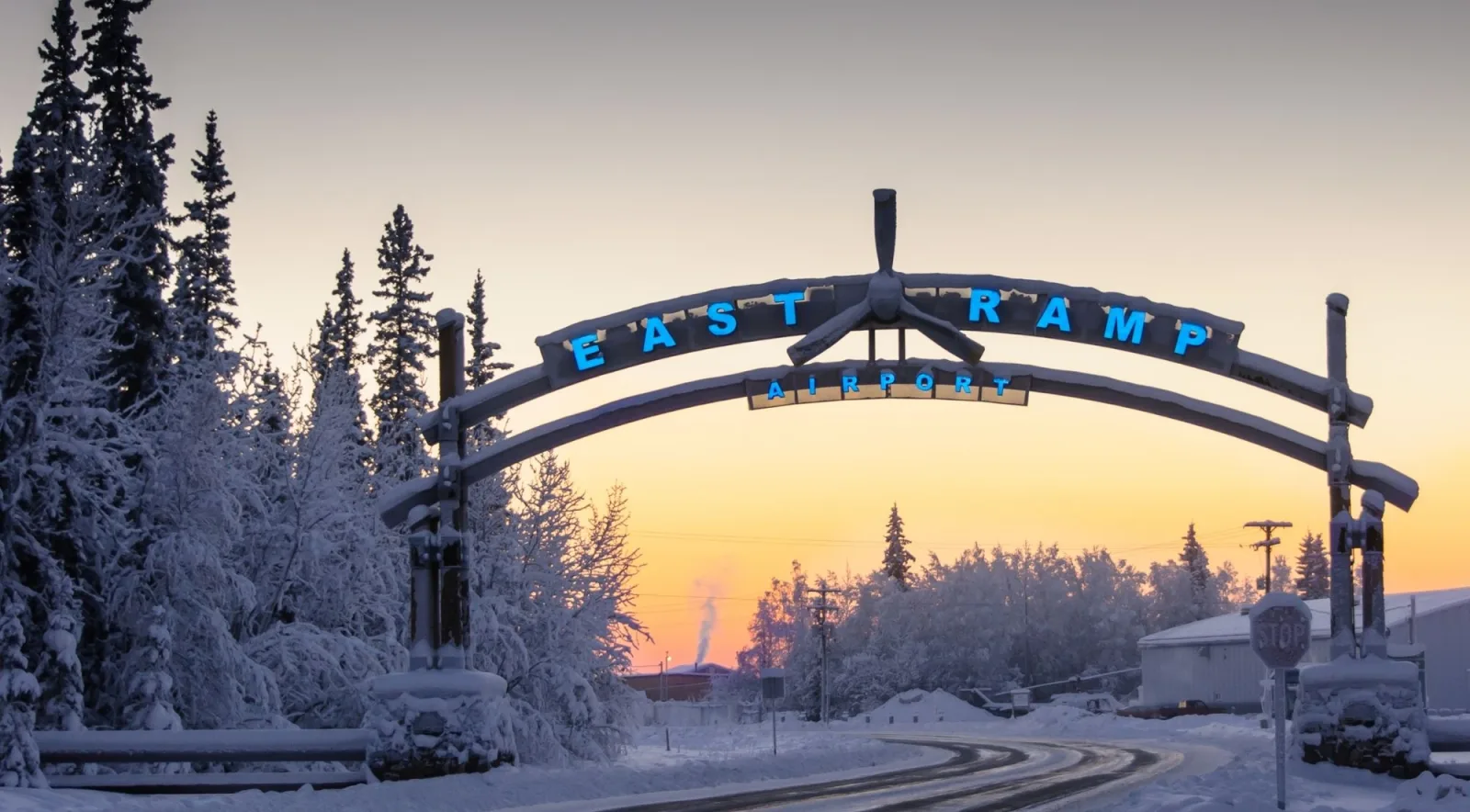 East Ramp airport entrance arch at sunset with snow-covered spruce trees